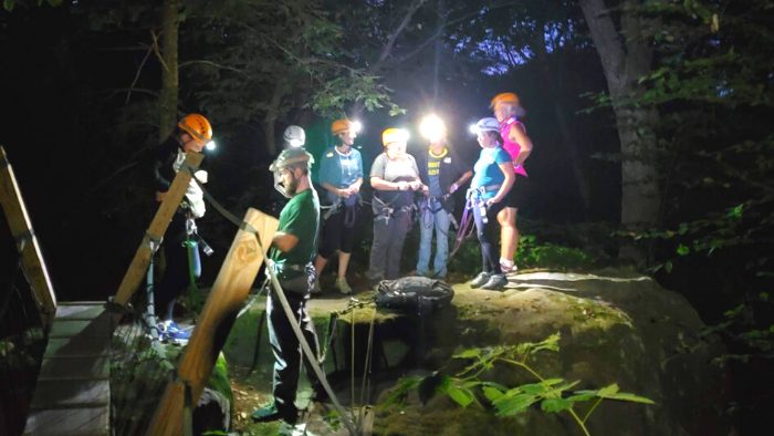 Women standing on a rock wearing headlamps at night during a rappelling trip in WV.