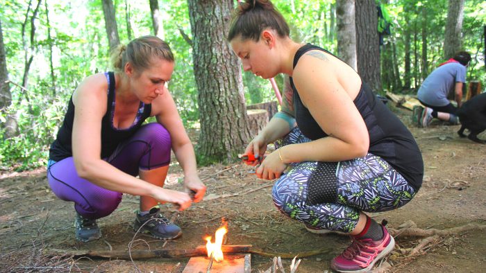 Two women kneeling down and building a fire during a survival training course in VA.