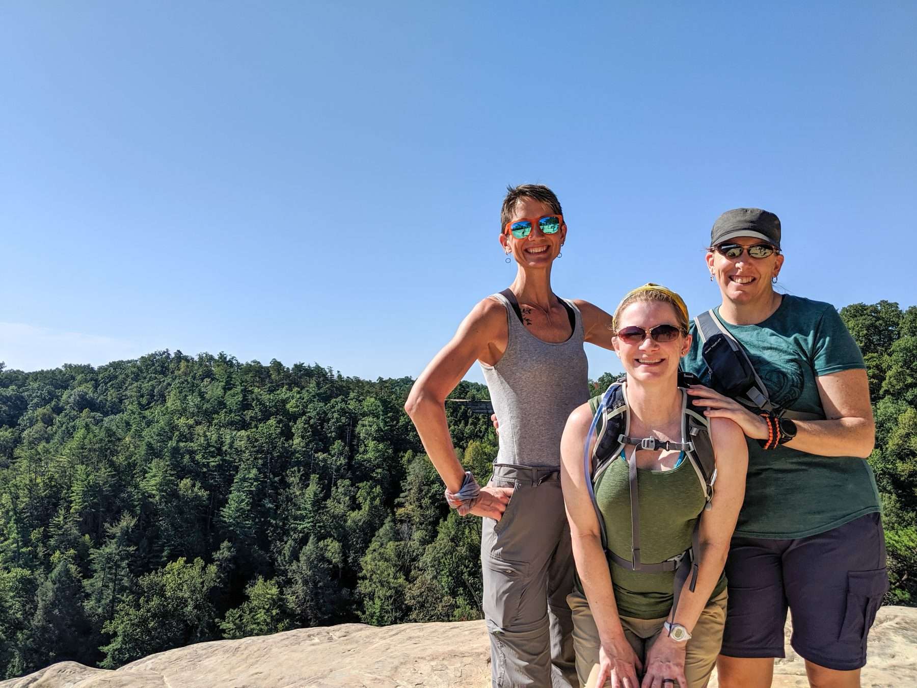 Three women smiling and posing in front of trees in Red River Gorge, Kentucky