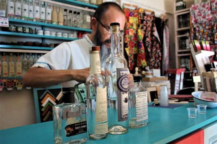 Man pouring a drink behind counter surrounded by mezcal bottles