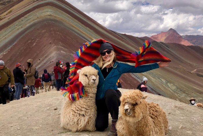 Woman with two llamans in front of Rainbow Mountain in Peru, during a tour.