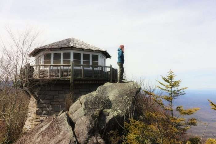 Woman in Great Smoky Mountains standing on rock next to fire tower.