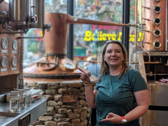 Woman pointing to a moonshine still during a trip to a distillery to learn about moonshine recipes and flavors.