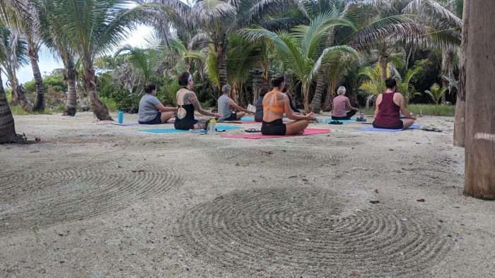 A small group of women sitting on beach doing yoga as part of a guided tour.