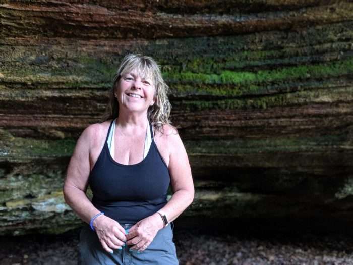 Woman smiling and posing in front of a large rock while backpacking in Red River Gorge