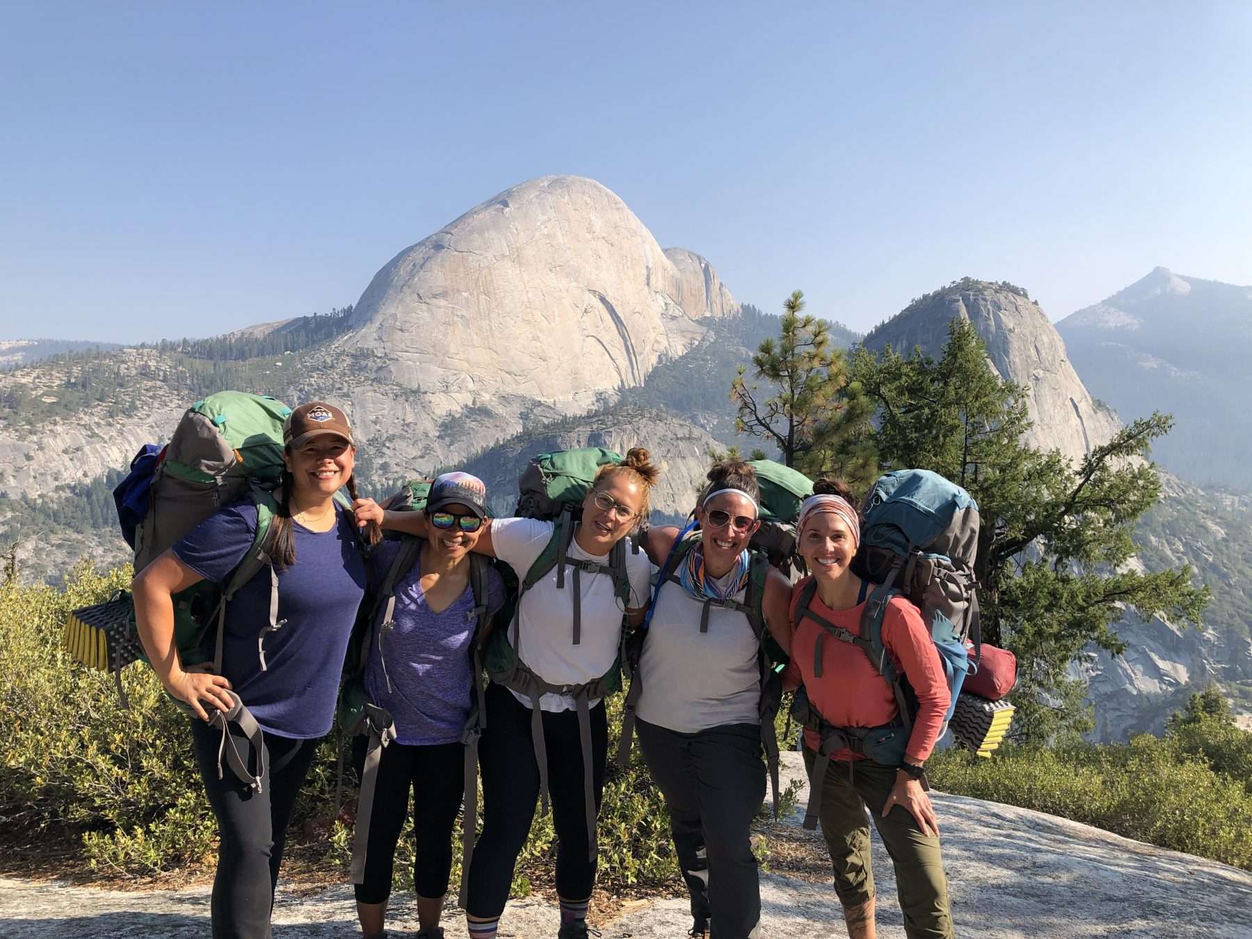Women posing in front of Half Dome wearing backpacks during a hike