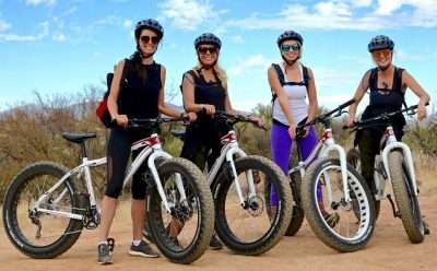 Women smiling and standing while holding fat tire bikes during a tour.