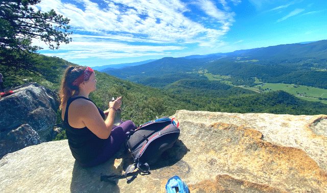 Woman sitting on rock next to outdoor gear gifts looking at trees and sky 