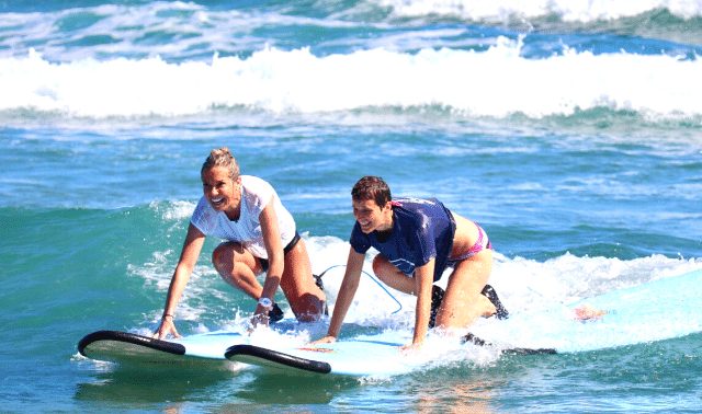 Two women traveling together riding on surfboards in the ocean 