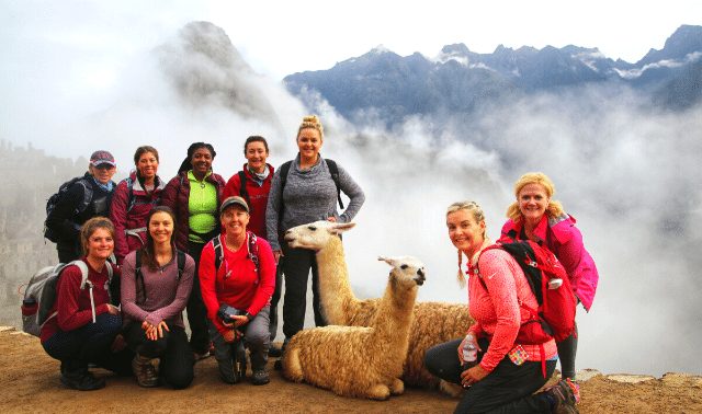 Women traveling together to Machu Picchu posing with llamas in front of foggy mountains