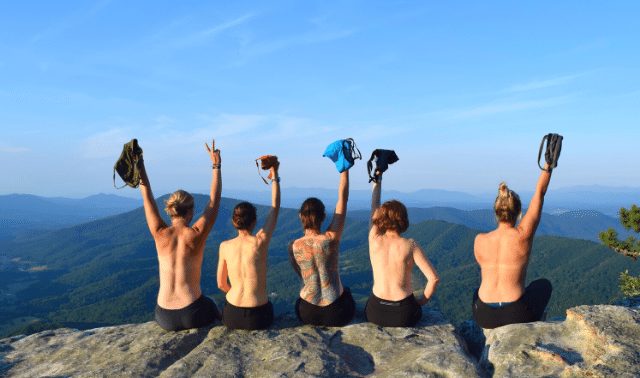 Women traveling together sitting on a rock and holding shirts up in air