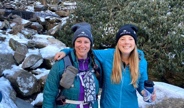 Two women in winter clothing posing in front of snowy rocks during a hiking trip