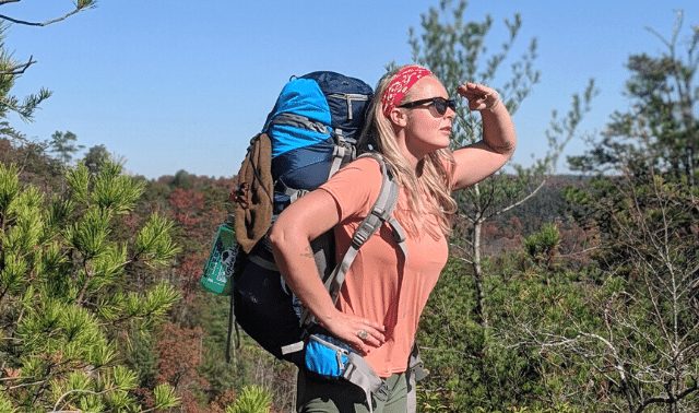 Woman wearing blue backpack and red bandana looking into the distance while safely hiking alone in Red River Gorge